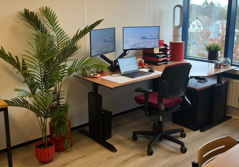 Kantoorruimte met bureaus, computers en uitzicht op groene omgeving.